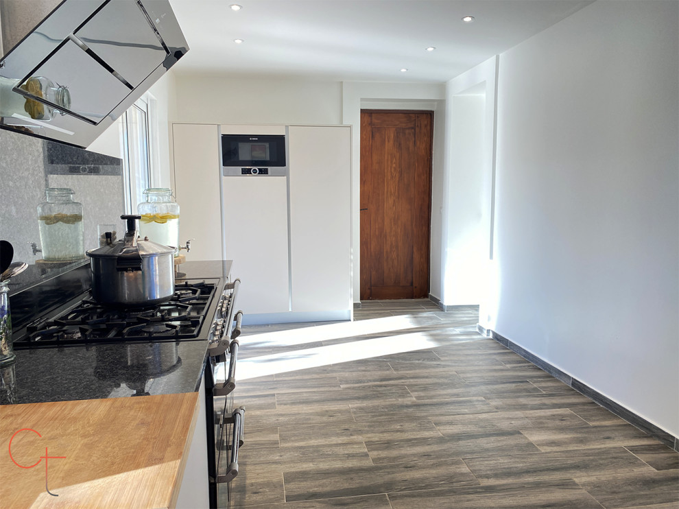This is an example of a large modern grey and black l-shaped open plan kitchen in Other with a double-bowl sink, flat-panel cabinets, beige cabinets, granite worktops, black splashback, granite splashback, integrated appliances, ceramic flooring, grey floors and black worktops.
