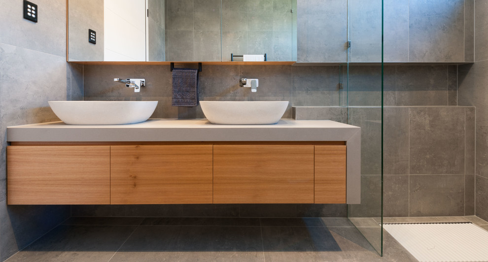 This is an example of a large contemporary master bathroom in Brisbane with light wood cabinets, a freestanding tub, a double shower, a wall-mount toilet, gray tile, ceramic tile, grey walls, ceramic floors, a console sink and engineered quartz benchtops.