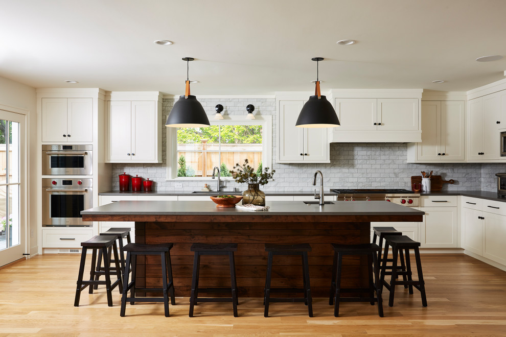 Transitional l-shaped kitchen in Minneapolis with shaker cabinets, white cabinets, grey splashback, subway tile splashback, stainless steel appliances, medium hardwood floors, with island and grey benchtop.
