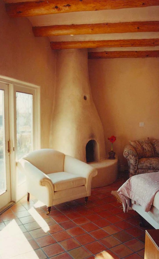 This is an example of a large master bedroom in Albuquerque with beige walls, terra-cotta floors, a corner fireplace and a plaster fireplace surround.