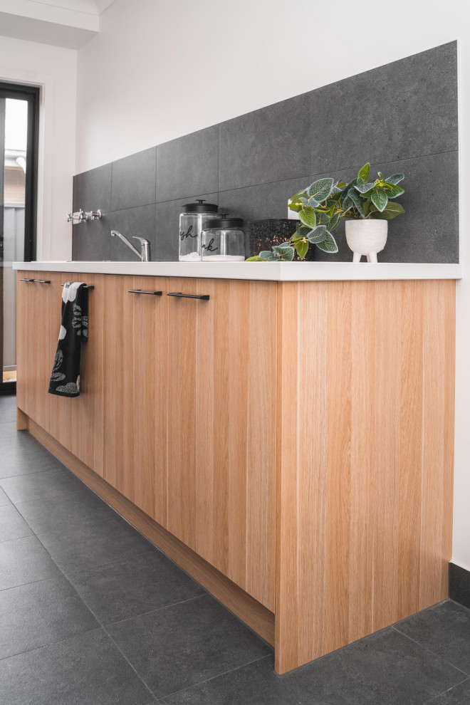 Cette photo montre une buanderie linéaire moderne en bois clair de taille moyenne avec un mur gris, un sol en carrelage de céramique et un sol gris.