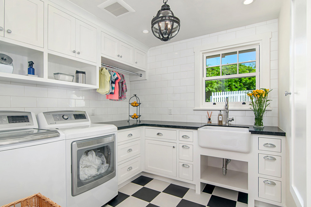 This is an example of a small traditional l-shaped dedicated laundry room in San Diego with a farmhouse sink, white cabinets, white walls, linoleum floors, a side-by-side washer and dryer, multi-coloured floor, black benchtop and shaker cabinets.