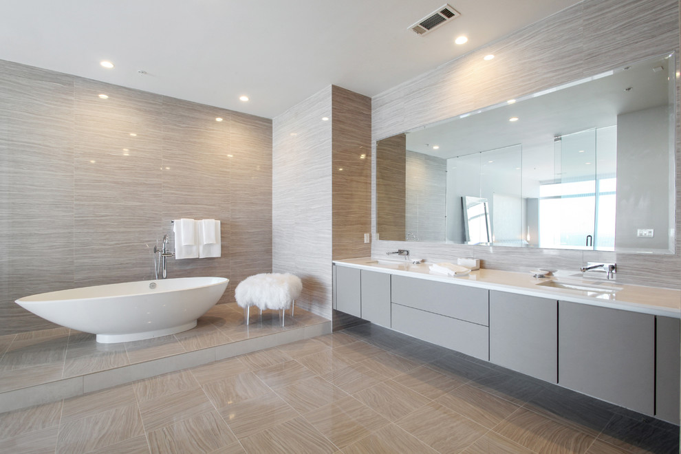 Photo of a contemporary master bathroom in Atlanta with flat-panel cabinets, grey cabinets, a freestanding tub, beige tile, beige walls, an undermount sink, beige floor and white benchtops.