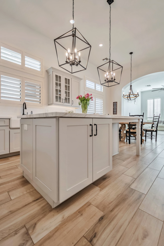Large transitional u-shaped porcelain tile, brown floor and exposed beam kitchen photo in Phoenix with a farmhouse sink, shaker cabinets, gray cabinets, quartzite countertops, white backsplash, porcelain backsplash, stainless steel appliances, an island and white countertops