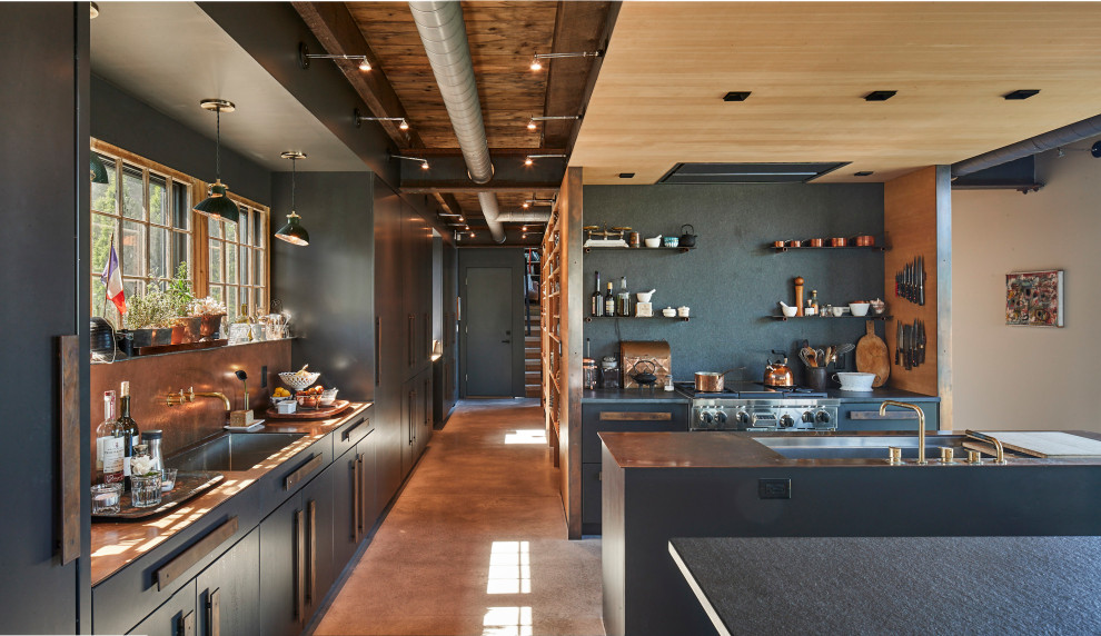 Photo of an industrial u-shaped kitchen in New York with an undermount sink, flat-panel cabinets, grey cabinets, grey splashback, stainless steel appliances, concrete floors, multiple islands, brown floor, grey benchtop and wood.