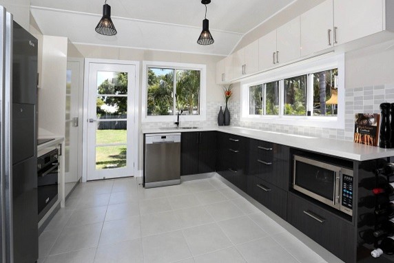 This is an example of a mid-sized transitional u-shaped kitchen in Townsville with a drop-in sink, flat-panel cabinets, solid surface benchtops, beige splashback, mosaic tile splashback, stainless steel appliances, ceramic floors and no island.