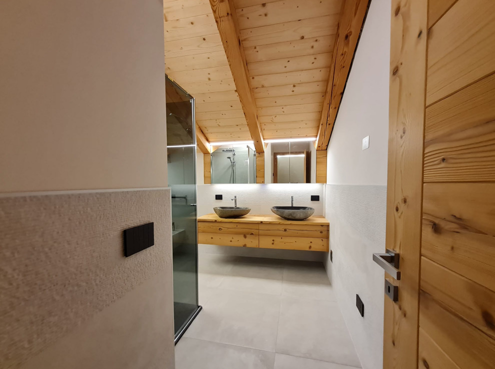 Mid-sized contemporary master bathroom in Other with brown cabinets, a corner shower, gray tile, marble, grey walls, a vessel sink, wood benchtops, grey floor, a hinged shower door, brown benchtops, a double vanity, exposed beam, a floating vanity, beaded inset cabinets and marble floors.