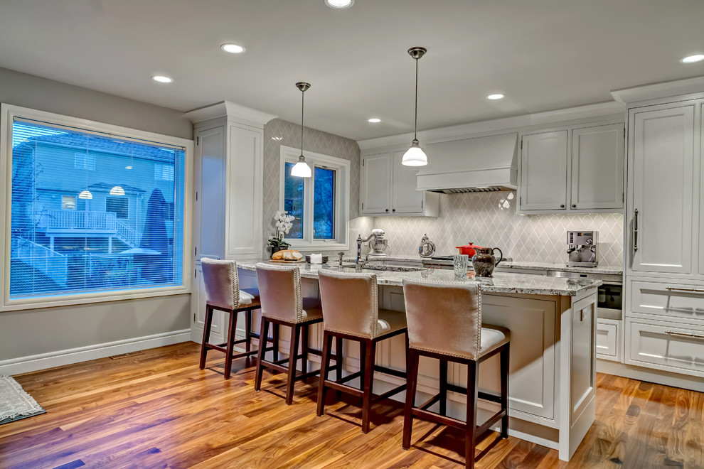 Open concept kitchen - mid-sized transitional single-wall medium tone wood floor open concept kitchen idea in Calgary with an undermount sink, white cabinets, shaker cabinets, granite countertops, gray backsplash, glass tile backsplash, stainless steel appliances and an island