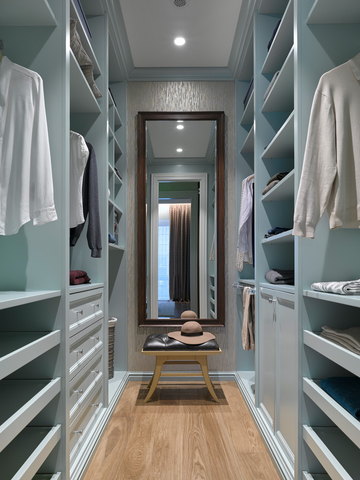 Small transitional gender-neutral walk-in wardrobe in Moscow with blue cabinets, medium hardwood floors, recessed-panel cabinets and brown floor.