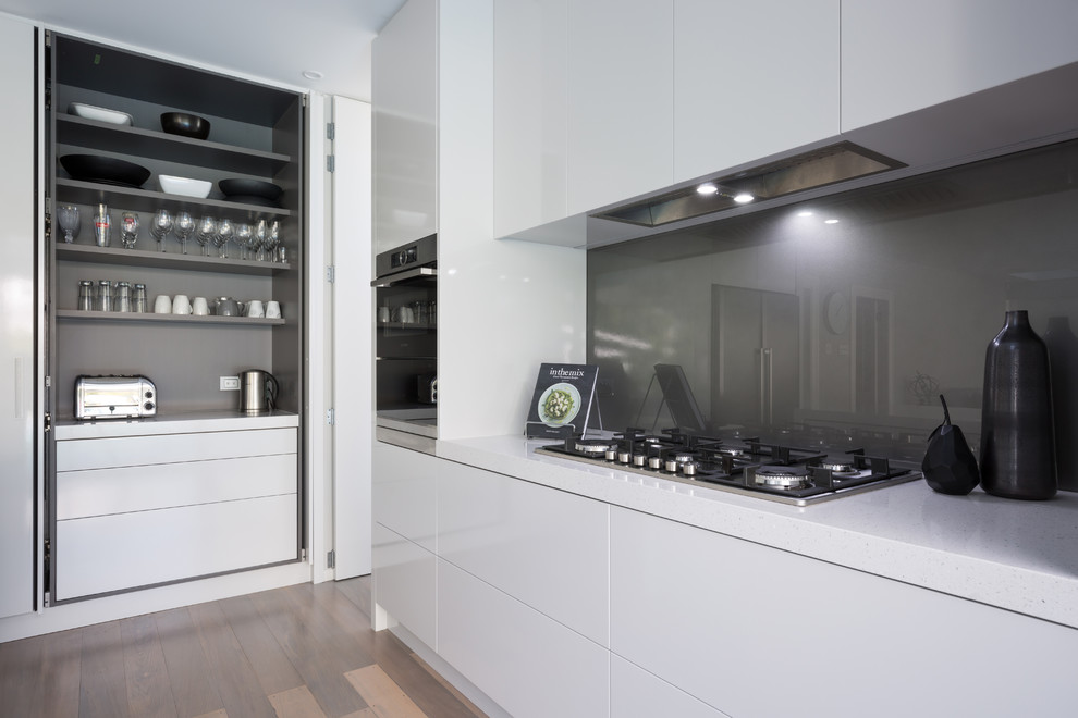 Inspiration for a large contemporary l-shaped eat-in kitchen in Auckland with an undermount sink, flat-panel cabinets, grey cabinets, quartz benchtops, grey splashback, glass sheet splashback, stainless steel appliances, light hardwood floors, with island and beige floor.