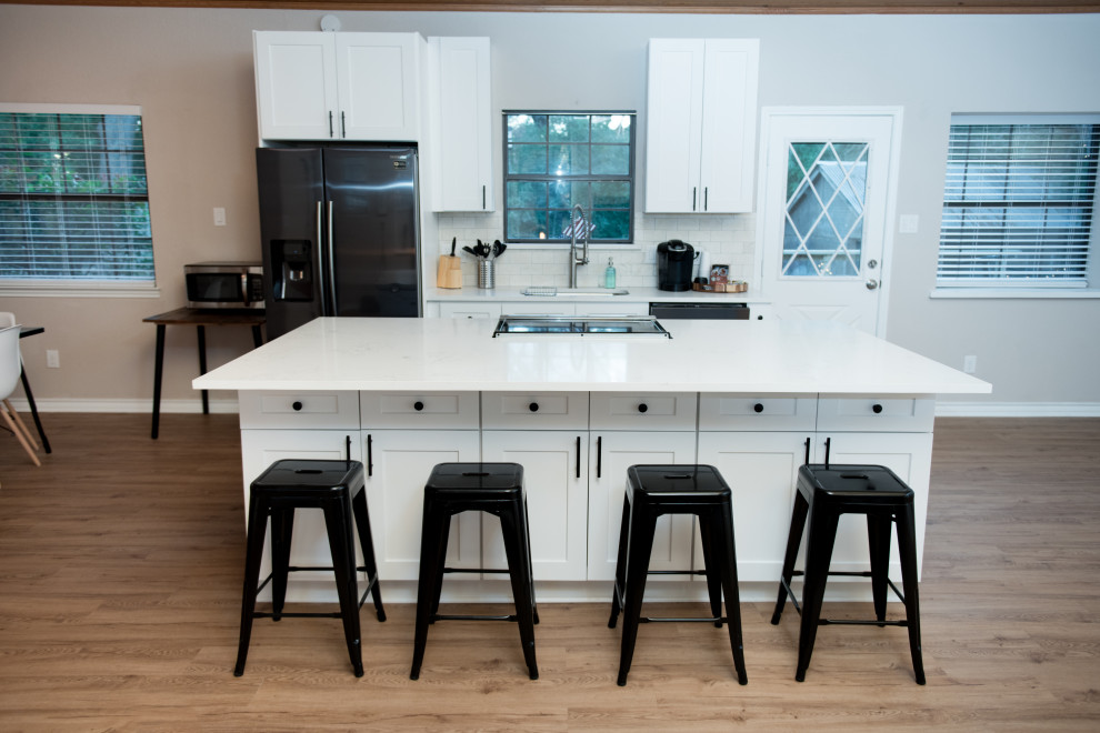 This is an example of a medium sized modern kitchen/diner in Dallas with a single-bowl sink, recessed-panel cabinets, white cabinets, quartz worktops, white splashback, ceramic splashback, stainless steel appliances, light hardwood flooring, an island, brown floors, white worktops and a wood ceiling.