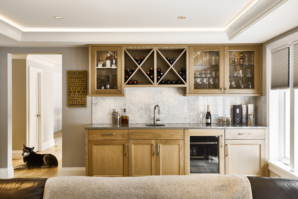 Design ideas for a mid-sized traditional single-wall wet bar in Other with glass-front cabinets, light wood cabinets, quartz benchtops, white splashback, light hardwood floors and grey benchtop.