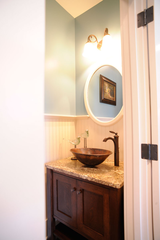 This is an example of a country powder room with shaker cabinets, medium wood cabinets, blue walls, a vessel sink, a freestanding vanity and panelled walls.