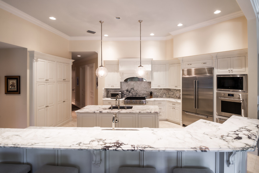 Large transitional u-shaped limestone floor and white floor open concept kitchen photo in Orlando with an undermount sink, raised-panel cabinets, white cabinets, marble countertops, gray backsplash, marble backsplash, stainless steel appliances and two islands