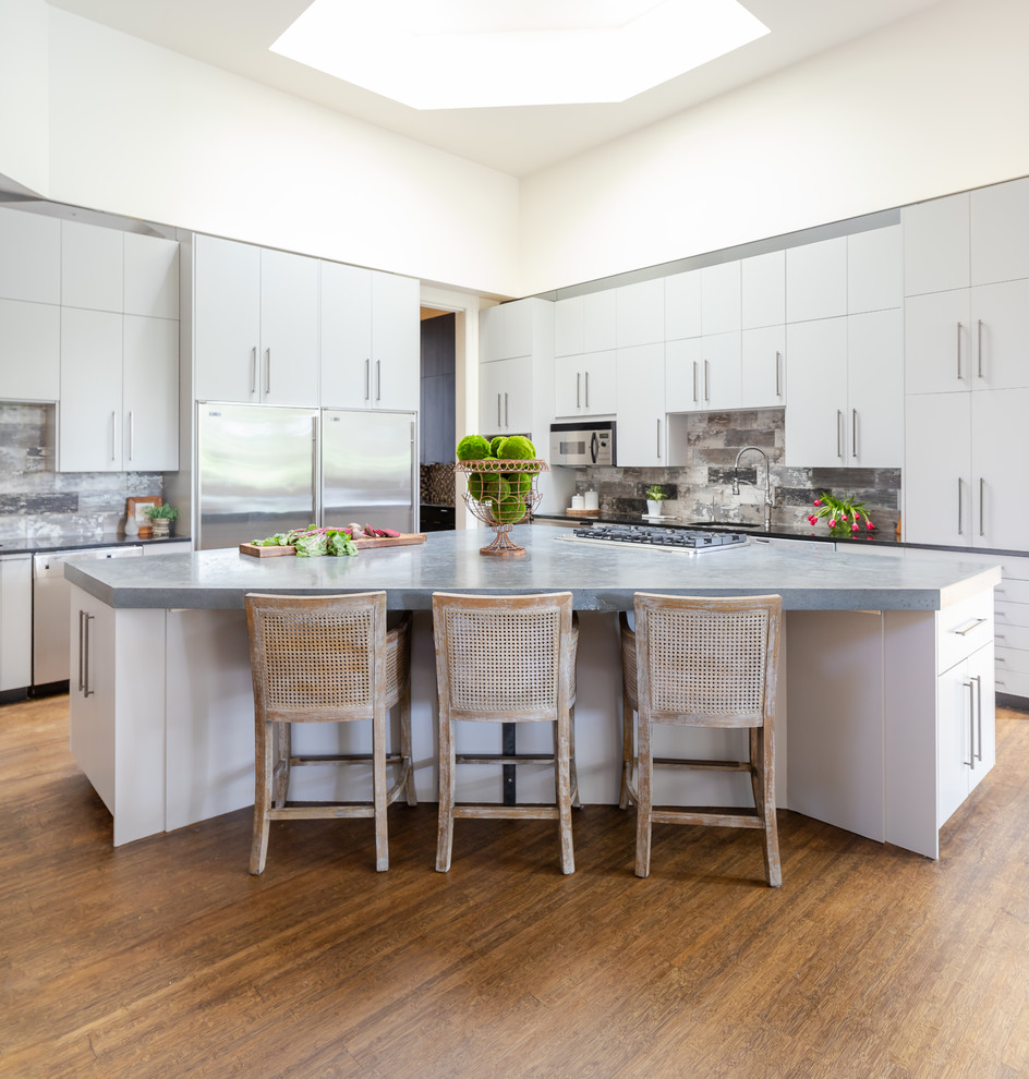 This is an example of a transitional l-shaped kitchen in Nashville with flat-panel cabinets, white cabinets, stainless steel appliances, medium hardwood floors, with island, brown floor and grey benchtop.