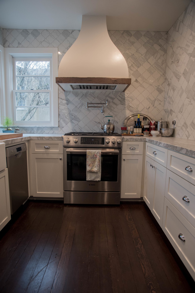 This is an example of a mid-sized country u-shaped kitchen in San Francisco with a farmhouse sink, shaker cabinets, white cabinets, quartzite benchtops, white splashback, glass tile splashback, stainless steel appliances, dark hardwood floors and no island.