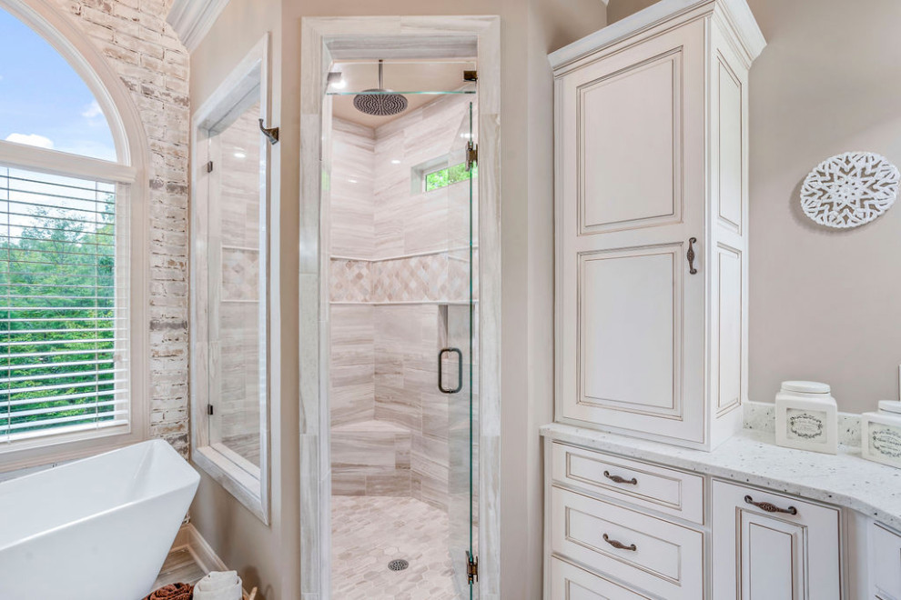 Свежая идея для дизайна: большая главная ванная комната в классическом стиле с фасадами островного типа, белыми фасадами, отдельно стоящей ванной, угловым душем, унитазом-моноблоком, серой плиткой, керамической плиткой, бежевыми стенами, полом из керамической плитки, врезной раковиной, столешницей из гранита, бежевым полом, душем с распашными дверями, белой столешницей, сиденьем для душа, тумбой под одну раковину, напольной тумбой, сводчатым потолком и кирпичными стенами - отличное фото интерьера