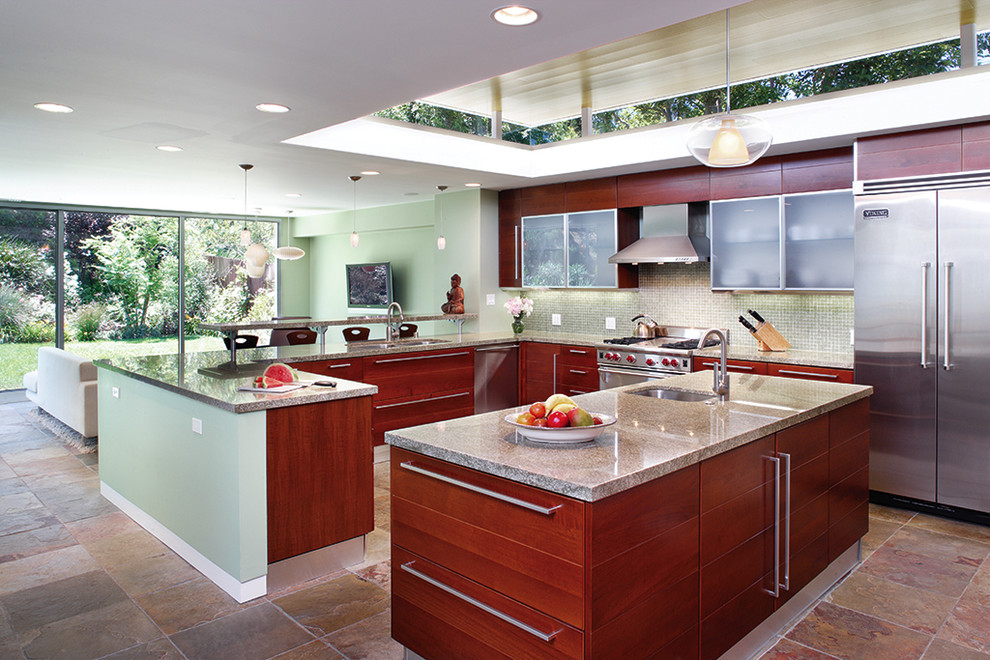 Mid-sized contemporary u-shaped open plan kitchen in Los Angeles with a double-bowl sink, flat-panel cabinets, medium wood cabinets, granite benchtops, green splashback, glass tile splashback, stainless steel appliances, slate floors, with island and green benchtop.