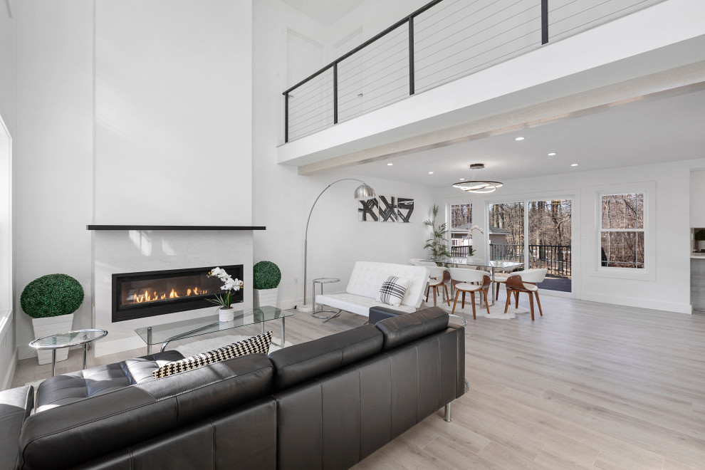 Inspiration for a large modern formal loft-style living room in Newark with white walls, light hardwood floors, a standard fireplace, a wood fireplace surround, a wall-mounted tv, brown floor, vaulted and panelled walls.