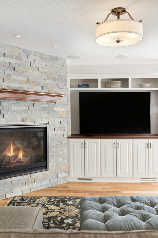 Inspiration for a mid-sized traditional look-out basement in Minneapolis with grey walls, light hardwood floors, a corner fireplace, a stone fireplace surround and brown floor.