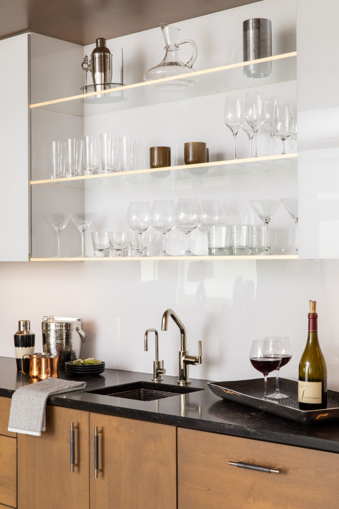 This is an example of a large modern single-wall wet bar in Minneapolis with an undermount sink, flat-panel cabinets, brown cabinets, granite benchtops, white splashback, multi-coloured floor and black benchtop.