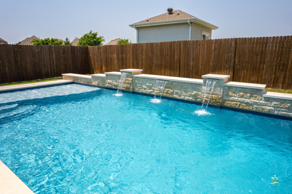 Modelo de piscina alargada de estilo americano de tamaño medio rectangular en patio trasero con paisajismo de piscina y losas de hormigón