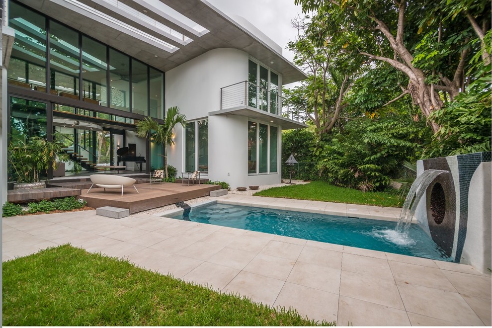 This is an example of a mid-sized contemporary backyard rectangular lap pool in Miami with a water feature and stamped concrete.