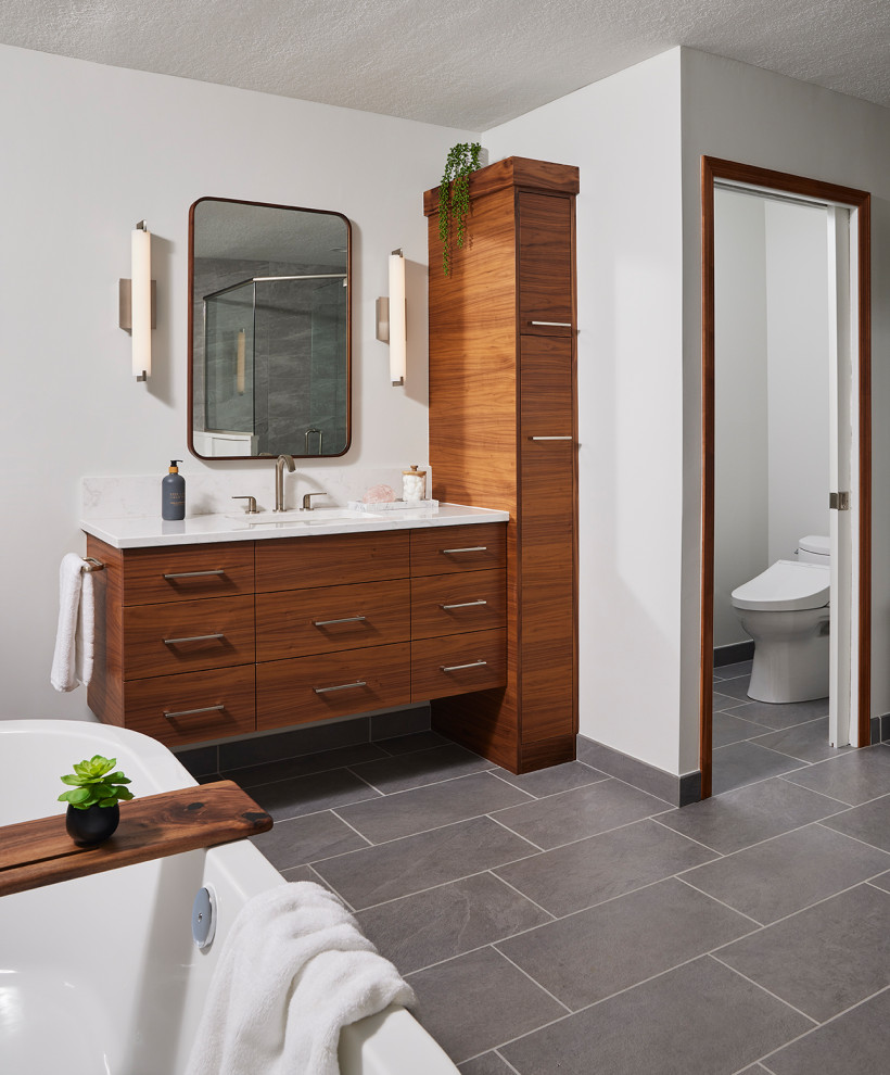 This is an example of a large modern bathroom in Minneapolis with flat-panel cabinets, medium wood cabinets, a freestanding tub, a corner shower, a bidet, gray tile, porcelain tile, white walls, porcelain floors, an undermount sink, engineered quartz benchtops, grey floor, a hinged shower door, white benchtops, an enclosed toilet, a single vanity and a floating vanity.