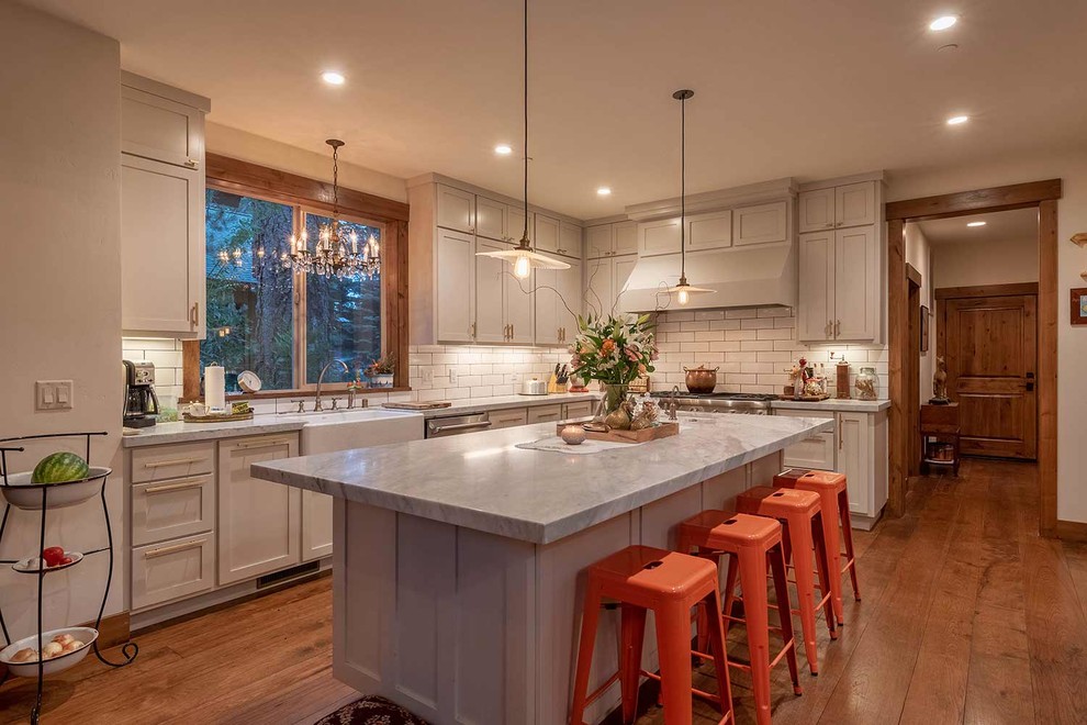 Design ideas for a large country l-shaped kitchen in Sacramento with a farmhouse sink, shaker cabinets, beige cabinets, marble benchtops, white splashback, subway tile splashback, stainless steel appliances, medium hardwood floors, with island, brown floor and grey benchtop.