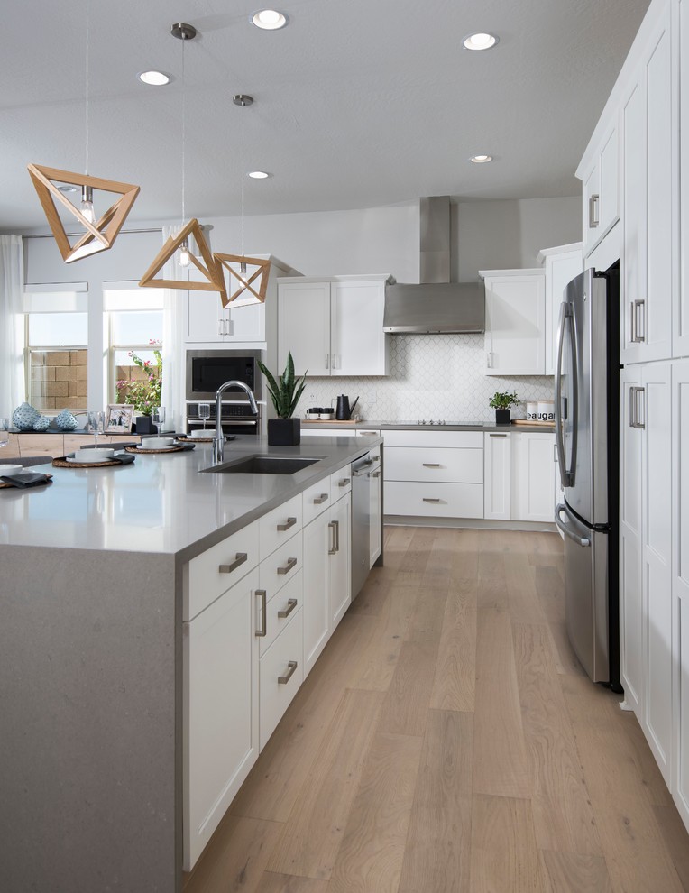 Contemporary l-shaped open plan kitchen in Phoenix with an undermount sink, shaker cabinets, white cabinets, quartz benchtops, white splashback, porcelain splashback, stainless steel appliances, light hardwood floors, with island, beige floor and grey benchtop.