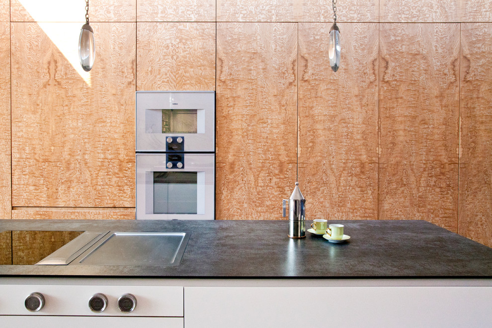 This is an example of a large modern galley eat-in kitchen in London with a double-bowl sink, flat-panel cabinets, white splashback, marble splashback, stainless steel appliances, with island, white floor and black benchtop.