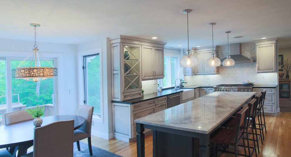 Photo of an expansive transitional u-shaped eat-in kitchen in Boston with a farmhouse sink, recessed-panel cabinets, grey cabinets, quartz benchtops, white splashback, stainless steel appliances, light hardwood floors and with island.