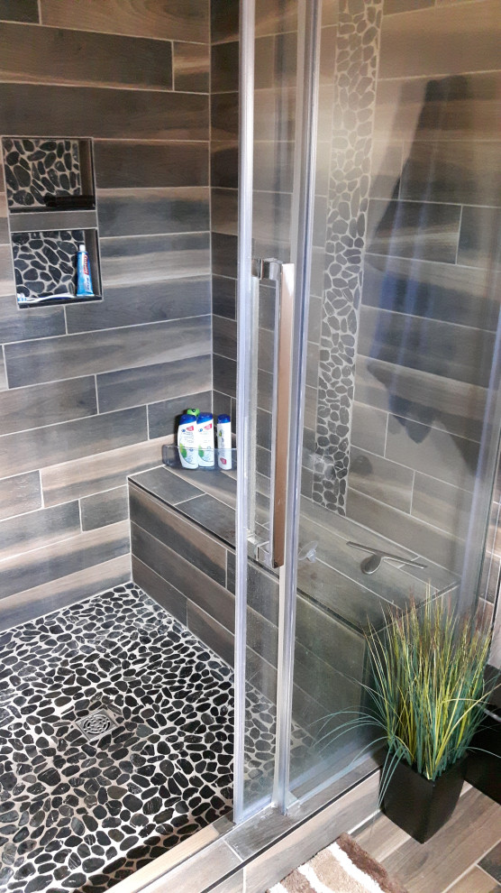 Amerikansk inredning av ett mellanstort brun brunt badrum med dusch, med öppna hyllor, svarta skåp, en dusch i en alkov, en toalettstol med separat cisternkåpa, grå kakel, porslinskakel, ett fristående handfat, träbänkskiva och dusch med skjutdörr