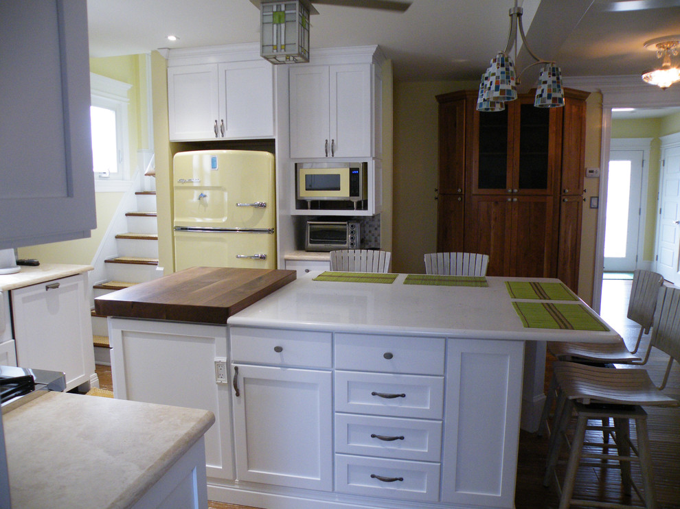 This is an example of a mid-sized traditional u-shaped eat-in kitchen in Philadelphia with a farmhouse sink, shaker cabinets, white cabinets, solid surface benchtops, multi-coloured splashback, mosaic tile splashback, coloured appliances, dark hardwood floors and with island.