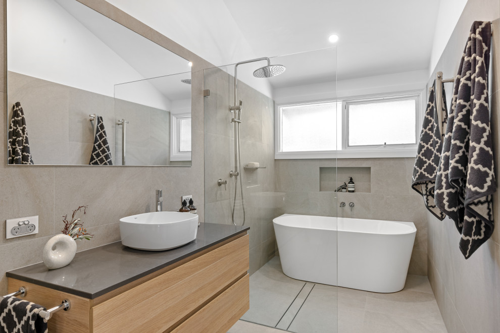 This is an example of a mid-sized contemporary master wet room bathroom in Sydney with flat-panel cabinets, light wood cabinets, a two-piece toilet, beige tile, beige walls, a vessel sink, beige floor, black benchtops, a niche, a single vanity, a floating vanity, a freestanding tub and an open shower.