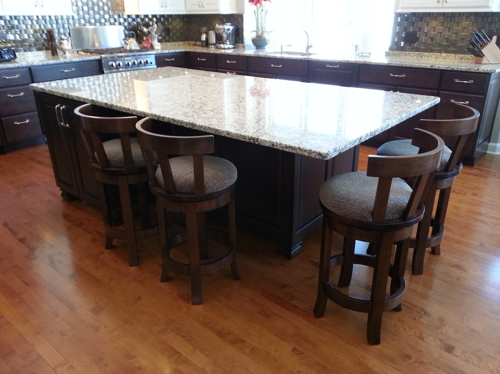 Kitchen - large transitional l-shaped medium tone wood floor and brown floor kitchen idea with an undermount sink, raised-panel cabinets, dark wood cabinets, granite countertops, metallic backsplash, stainless steel appliances and an island