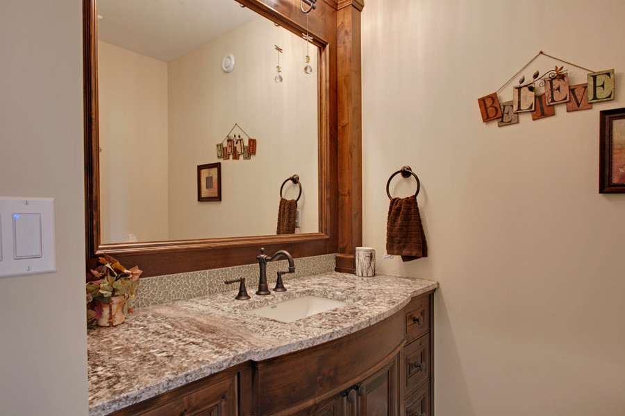 Mid-sized country powder room in Calgary with an undermount sink, raised-panel cabinets, dark wood cabinets, granite benchtops, beige tile, glass tile and beige walls.