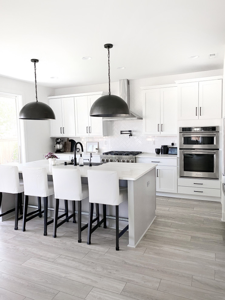Idéer för att renovera ett stort funkis vit vitt kök, med en undermonterad diskho, skåp i shakerstil, vita skåp, bänkskiva i kvarts, vitt stänkskydd, stänkskydd i porslinskakel, rostfria vitvaror, laminatgolv, en köksö och grått golv