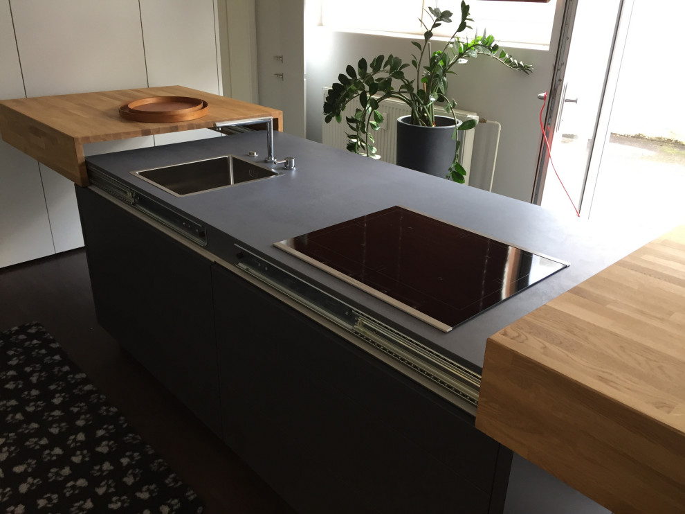 Einzeilige, Kleine Moderne Küche mit Einbauwaschbecken, flächenbündigen Schrankfronten, schwarzen Schränken, Arbeitsplatte aus Holz, schwarzen Elektrogeräten, Kücheninsel und brauner Arbeitsplatte in Sonstige