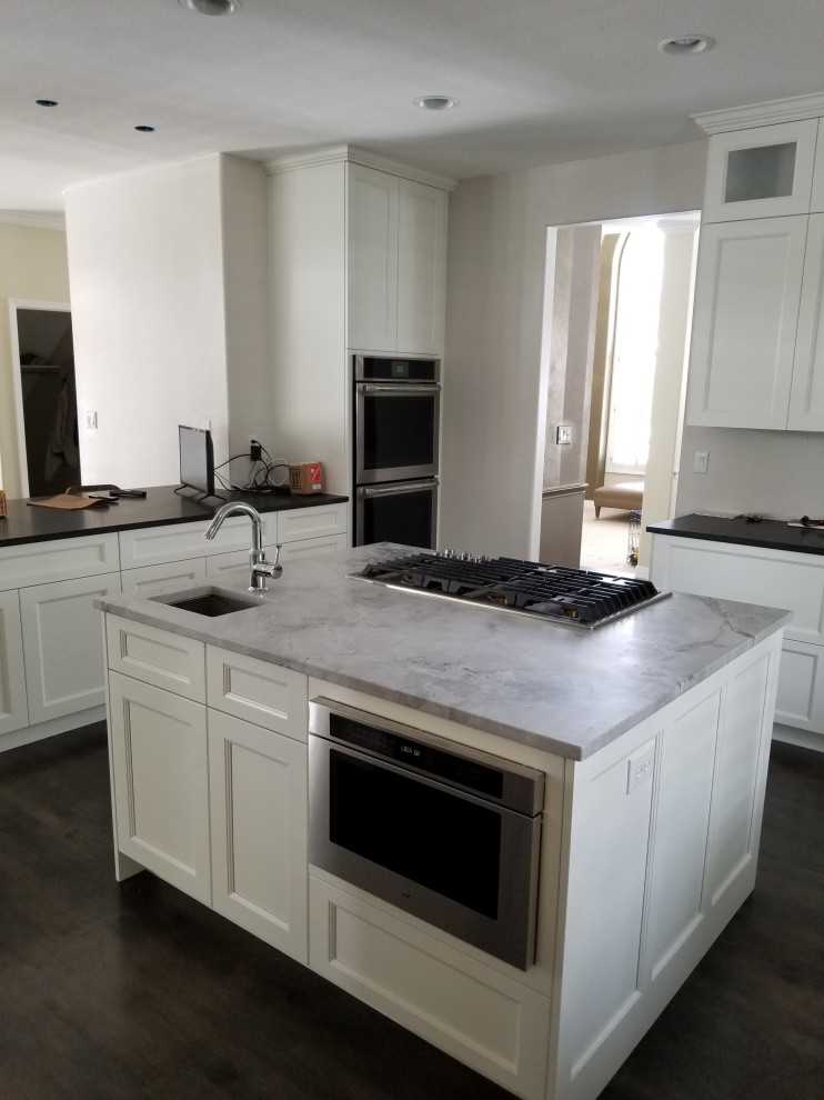 Example of a large transitional u-shaped dark wood floor and brown floor eat-in kitchen design in Denver with an undermount sink, shaker cabinets, white cabinets, quartz countertops, stainless steel appliances, an island and black countertops