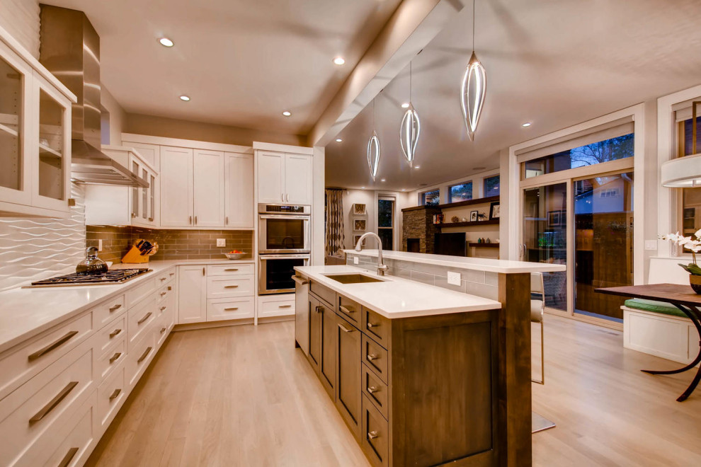Contemporary l-shaped open plan kitchen in Denver with shaker cabinets, white cabinets, engineered stone countertops, grey splashback, metro tiled splashback, stainless steel appliances, light hardwood flooring, an island and white worktops.