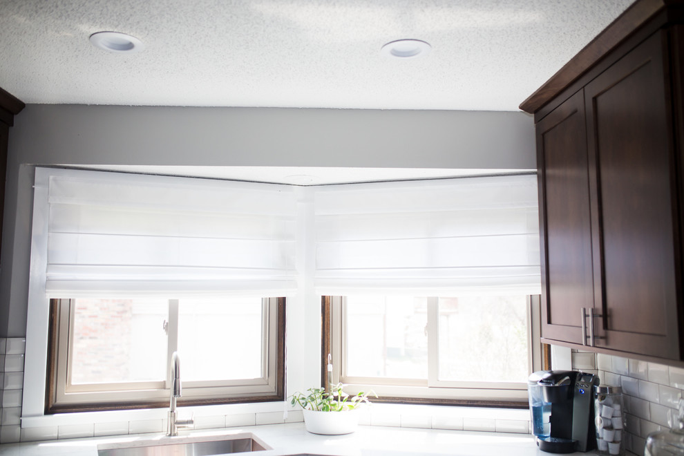 Example of a mid-sized transitional u-shaped medium tone wood floor and brown floor enclosed kitchen design in Omaha with shaker cabinets, dark wood cabinets, quartz countertops, white backsplash, subway tile backsplash, stainless steel appliances, a peninsula and an undermount sink