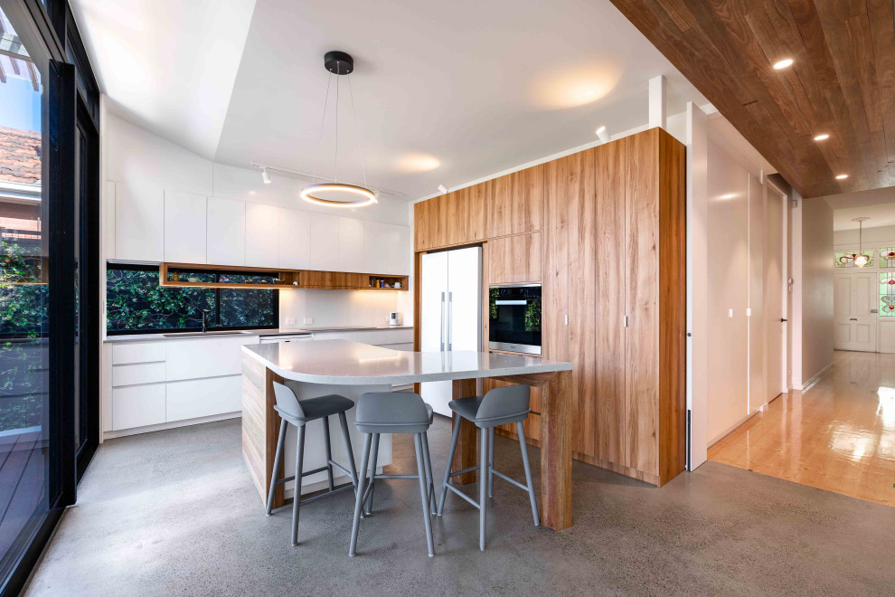 Inspiration for a contemporary open plan kitchen in Melbourne with an undermount sink, flat-panel cabinets, white cabinets, window splashback, concrete floors, with island, grey floor and grey benchtop.