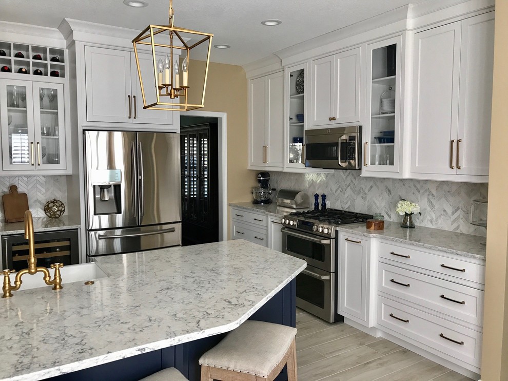 This is an example of a large transitional l-shaped open plan kitchen in Other with a farmhouse sink, beaded inset cabinets, white cabinets, quartz benchtops, white splashback, ceramic splashback, stainless steel appliances, ceramic floors, with island and grey floor.