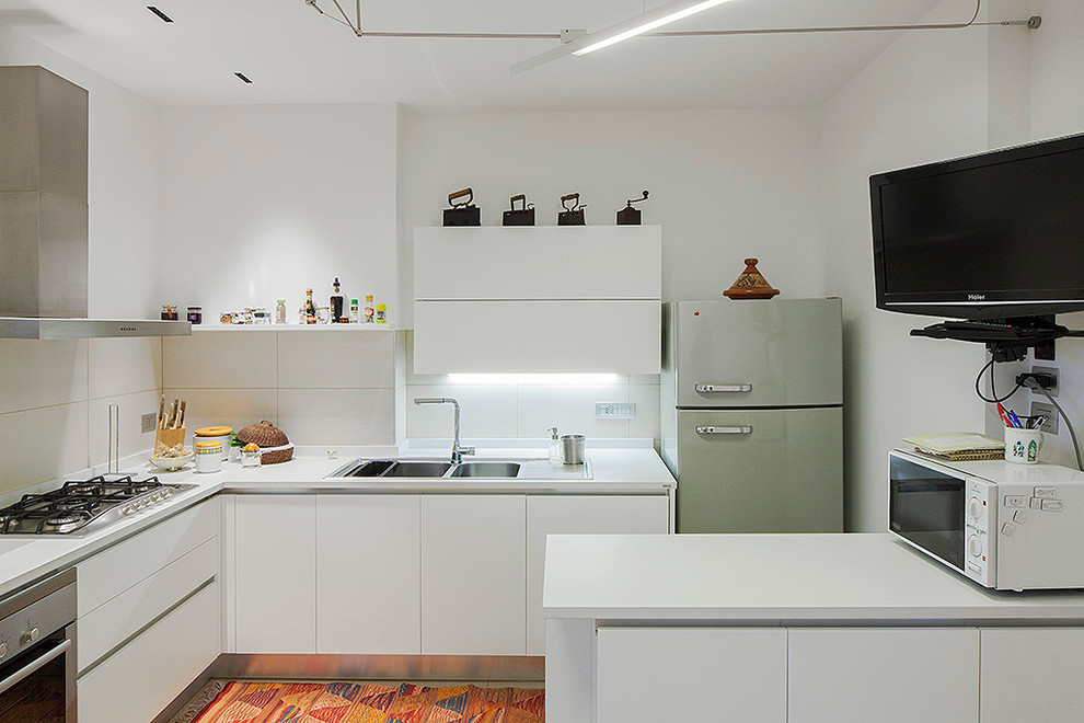 Photo of a mid-sized contemporary l-shaped kitchen in Catania-Palermo with a drop-in sink, flat-panel cabinets, white cabinets, solid surface benchtops, white splashback, ceramic splashback, stainless steel appliances and a peninsula.