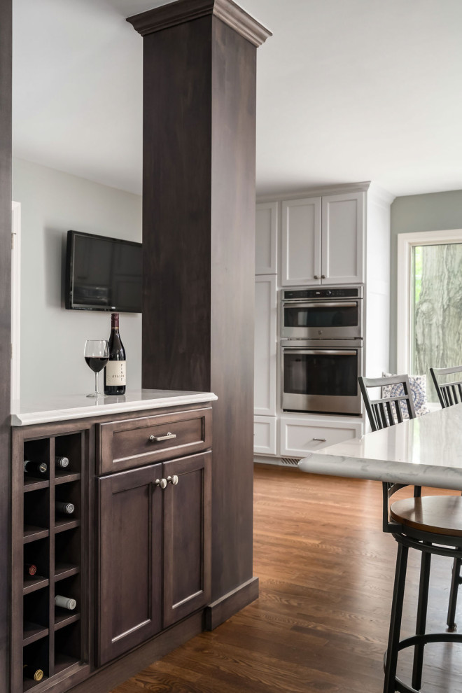 Small traditional single-wall home bar in Columbus with shaker cabinets, brown cabinets, quartz benchtops, medium hardwood floors, brown floor and white benchtop.