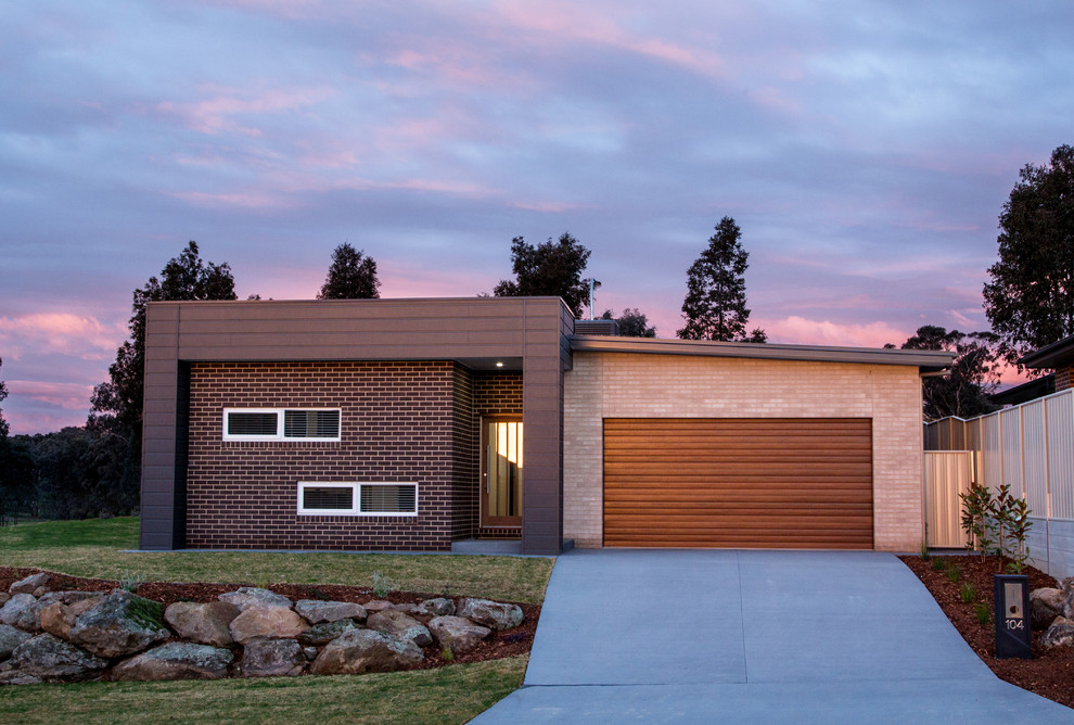 Photo of a mid-sized contemporary one-storey brick brown house exterior in Other with a flat roof and a metal roof.