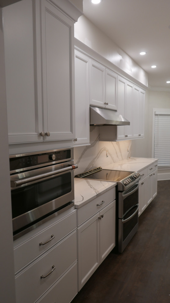 Mid-sized transitional galley laminate floor and brown floor eat-in kitchen photo with a farmhouse sink, shaker cabinets, white cabinets, quartz countertops, white backsplash, quartz backsplash, stainless steel appliances and white countertops