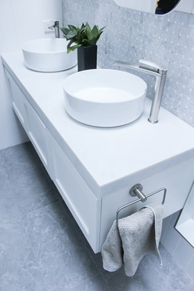 Photo of a medium sized modern ensuite bathroom in Perth with shaker cabinets, white cabinets, a walk-in shower, a one-piece toilet, white tiles, ceramic tiles, white walls, porcelain flooring, a vessel sink, marble worktops, grey floors, an open shower, white worktops, double sinks, a floating vanity unit and wainscoting.