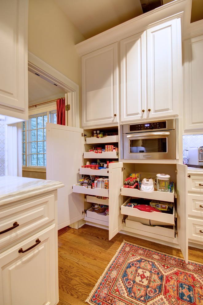 Large elegant l-shaped light wood floor eat-in kitchen photo in Austin with raised-panel cabinets, white cabinets, marble countertops, white backsplash, glass tile backsplash, stainless steel appliances and an island